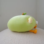 A light green plush toy shaped like an apple, resting on a textured cream surface against a plain light gray wall.