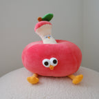 A cute plush toy shaped like a red apple with the core sticking out of it, featuring large cartoon eyes, a small yellow beak, and yellow feet, sitting on a textured white surface against a neutral gray background.
