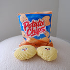 A novelty plush toy set shaped like a bag of potato chips and two potato chip characters, displayed on a soft, light-colored textured surface against a neutral gray background.