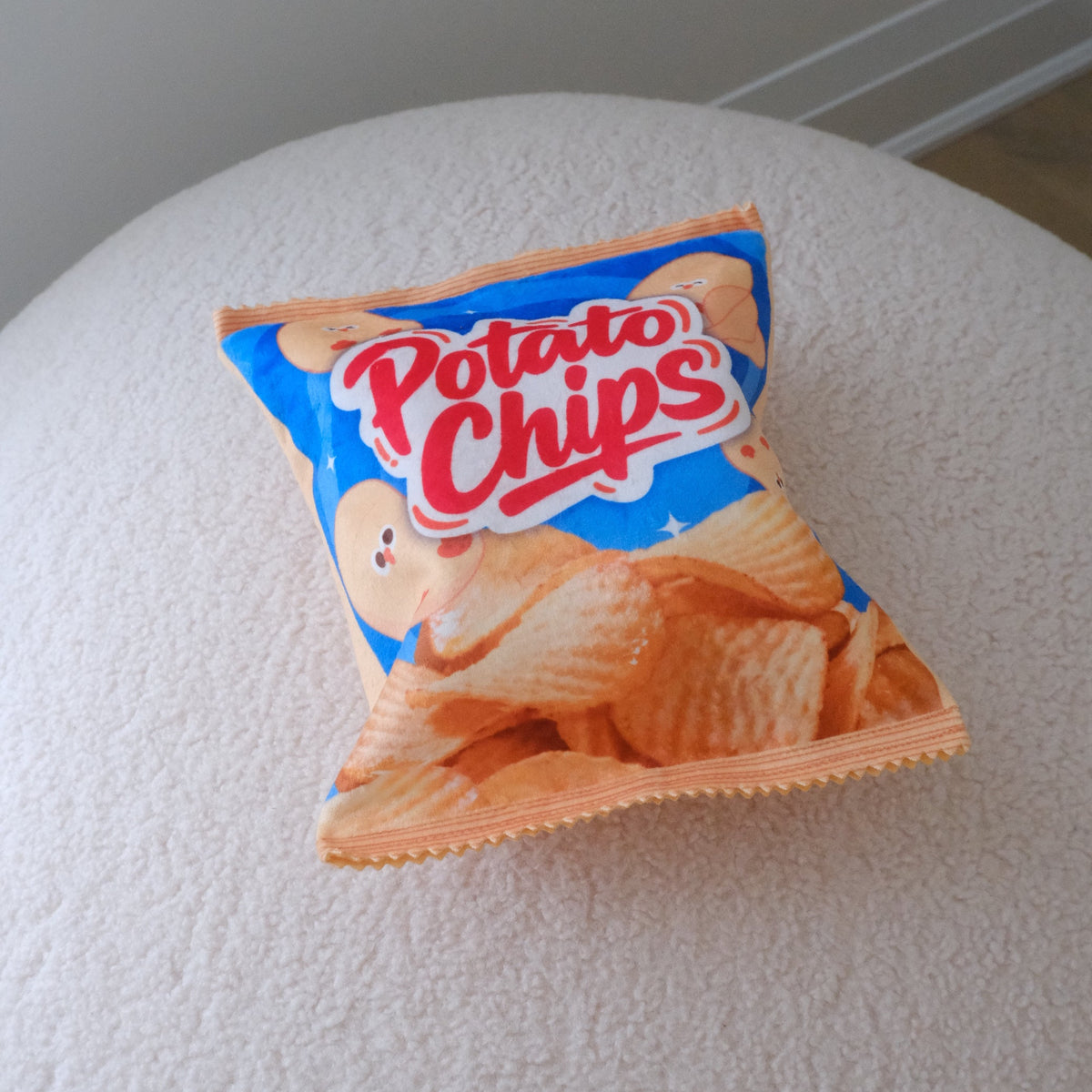 A miniature bag of potato chips resting on a textured white surface against a neutral gray background.