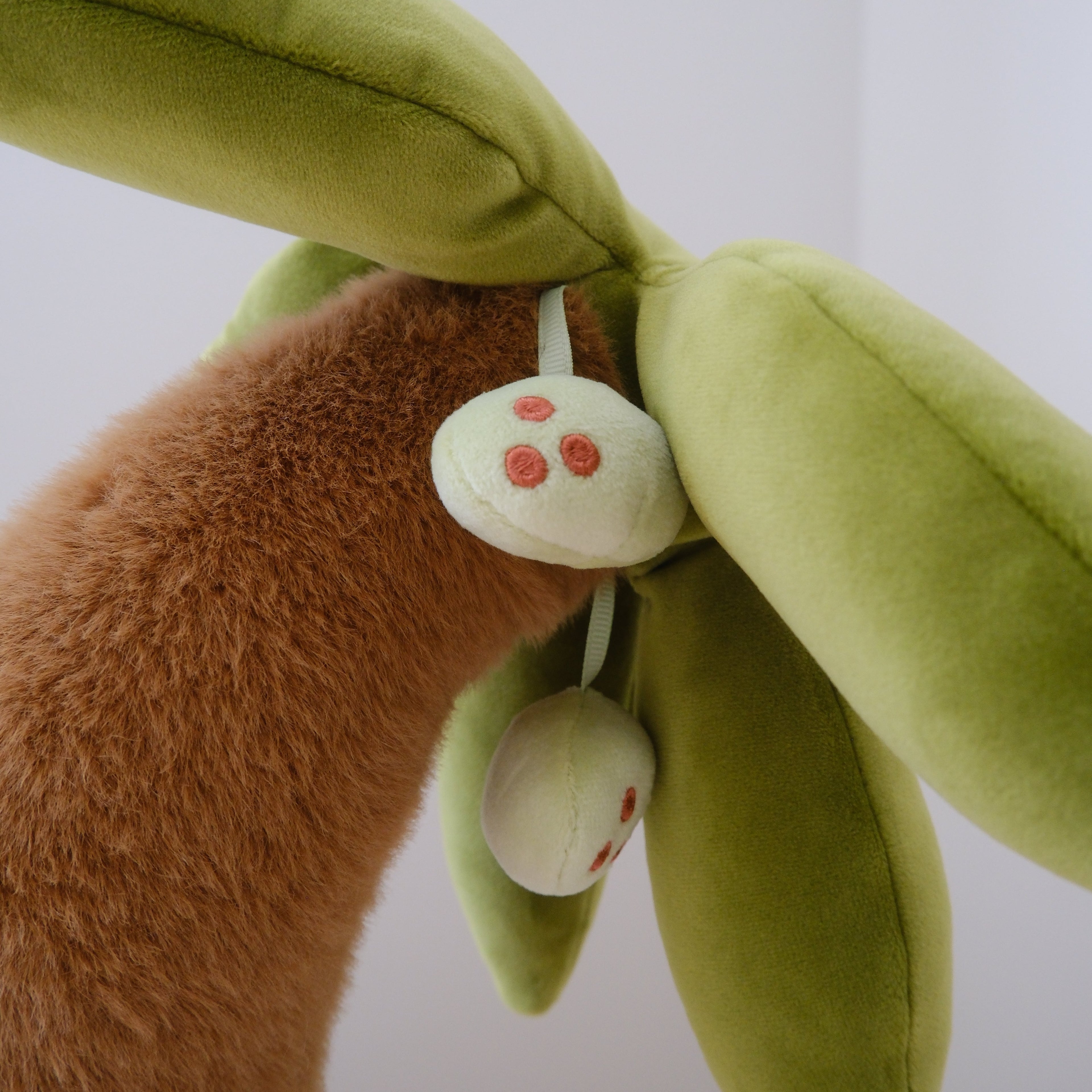 A close-up of a plush coconut tree toy with green leaves and hanging young coconut-shaped ornaments, shown against a plain light background.