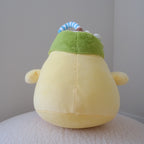 A yellow plush toy with a green coconut hat and a blue-and-white striped straw, photographed from the back against a plain indoor wall.