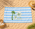 A beach towel laid flat on sandy ground, featuring light blue and white horizontal stripes with a green palm tree, coconuts, and a speech bubble that reads 'Fun dun'. Surrounding props include a straw hat, sunglasses, a woven basket, a starfish, and palm leaves.