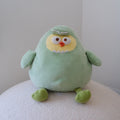 A light green plush dinosaur toy with a yellow face, white eyes, and a small orange beak, sitting on a textured white surface against a plain light gray background.