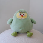 A light green plush dinosaur toy with a yellow face, white eyes, and a small orange beak, sitting on a textured white surface against a plain light gray background.