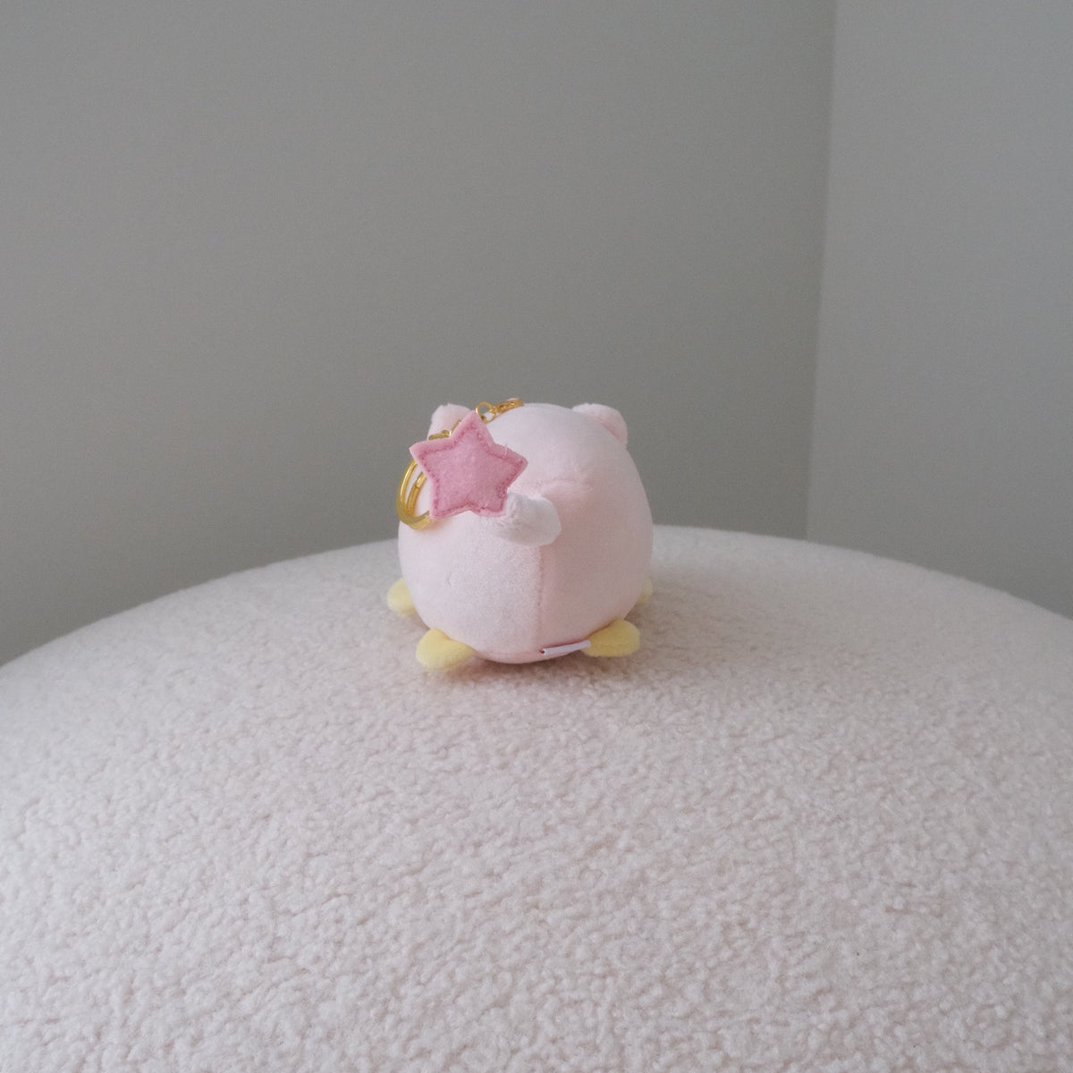 Back view of a yellow chicken plush in a pink pig costume with a star tipped tail and a gold keychain attachment