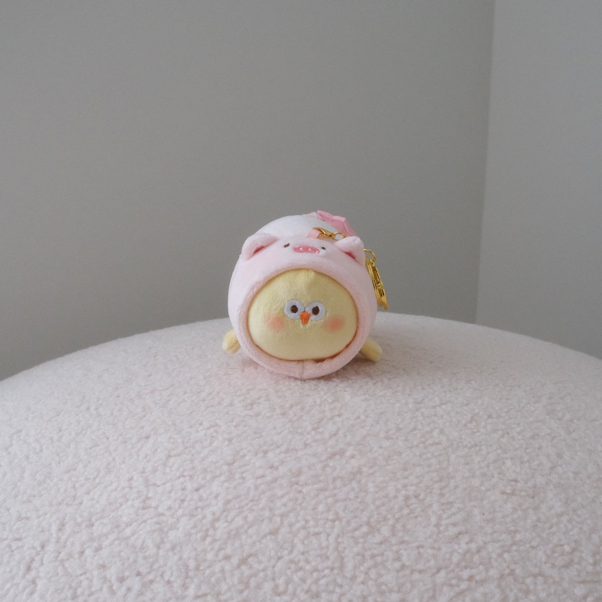 Yellow chicken plush in a pink pig costume with a gold keychain attachment