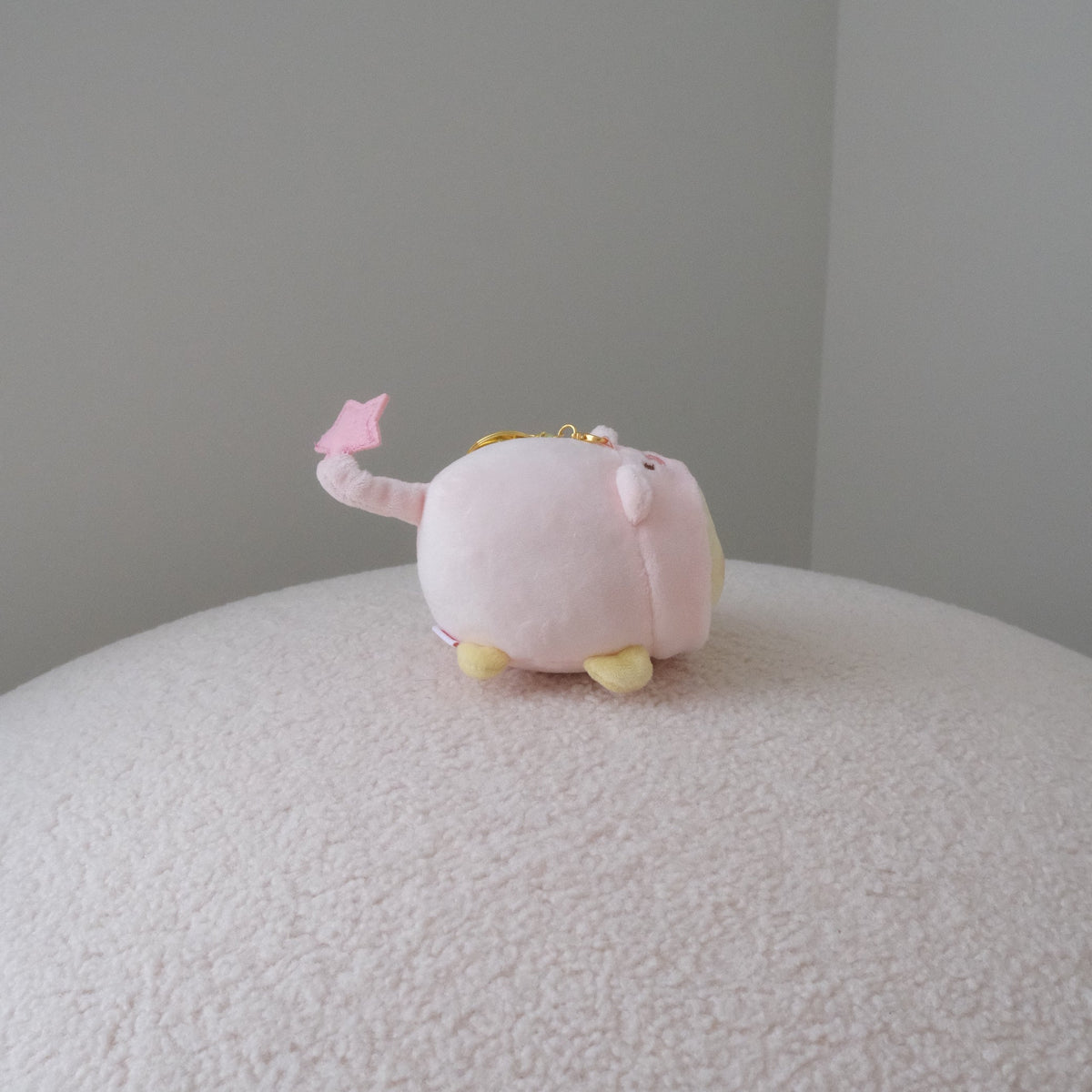 Back view of a yellow chicken plush in a pink pig costume with a star tipped tail and a gold keychain attachment