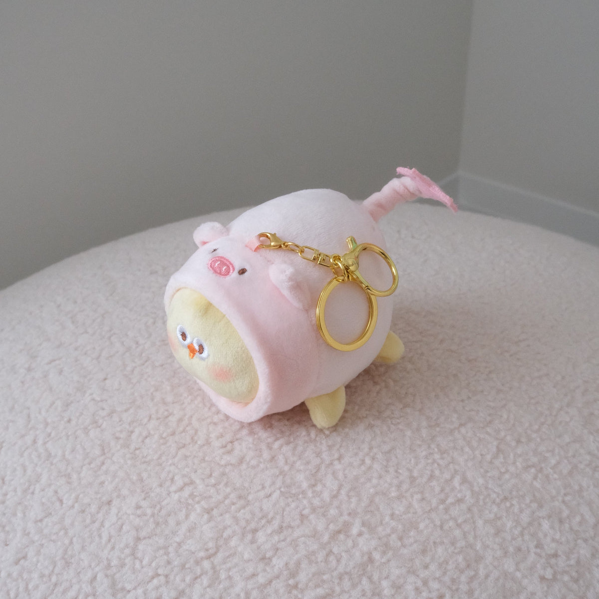 Back view of a yellow chicken plush in a pink pig costume with a star tipped tail and a gold keychain attachment