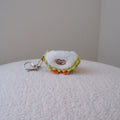A small plush keychain shaped like a quarter of a durian with embroidered eyes and a yellow-green stitched border, attached to a silver metal key ring, resting on a textured cream surface against a plain light gray wall.