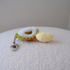 A small plush durian keychain resting on a textured white surface. The keychain features a yellow plush durian pulp attached to a green and white plush durian shell with a  silver metal clasp.