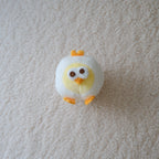 A small plush chick toy with a white body, yellow face, and orange beak and feet, lying on a textured off-white carpet.
