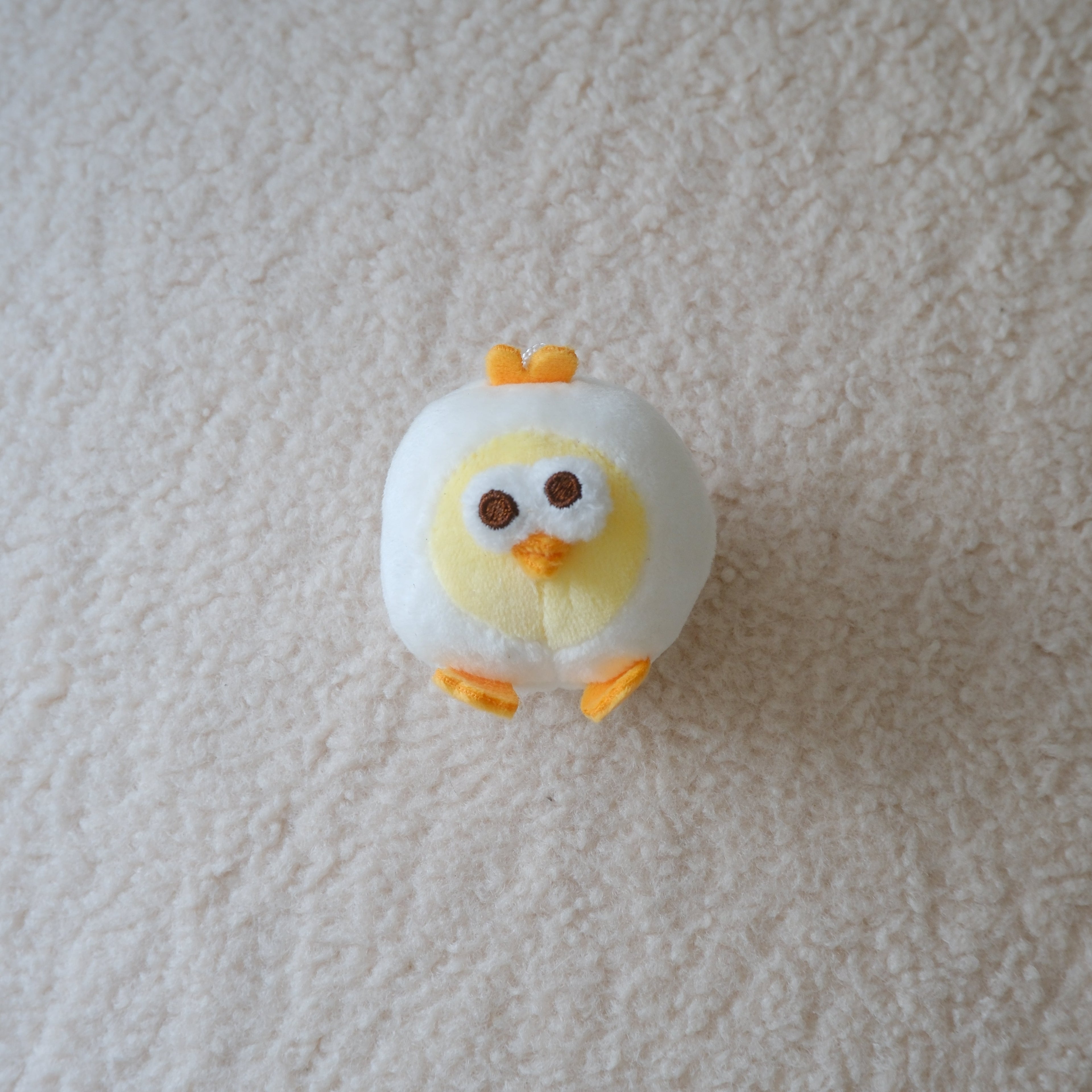 A small plush chick toy with a white body, yellow face, and orange beak and feet, lying on a textured off-white carpet.