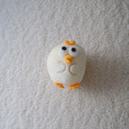A small white chick figurine with orange beak and feet placed on a textured white fabric background.