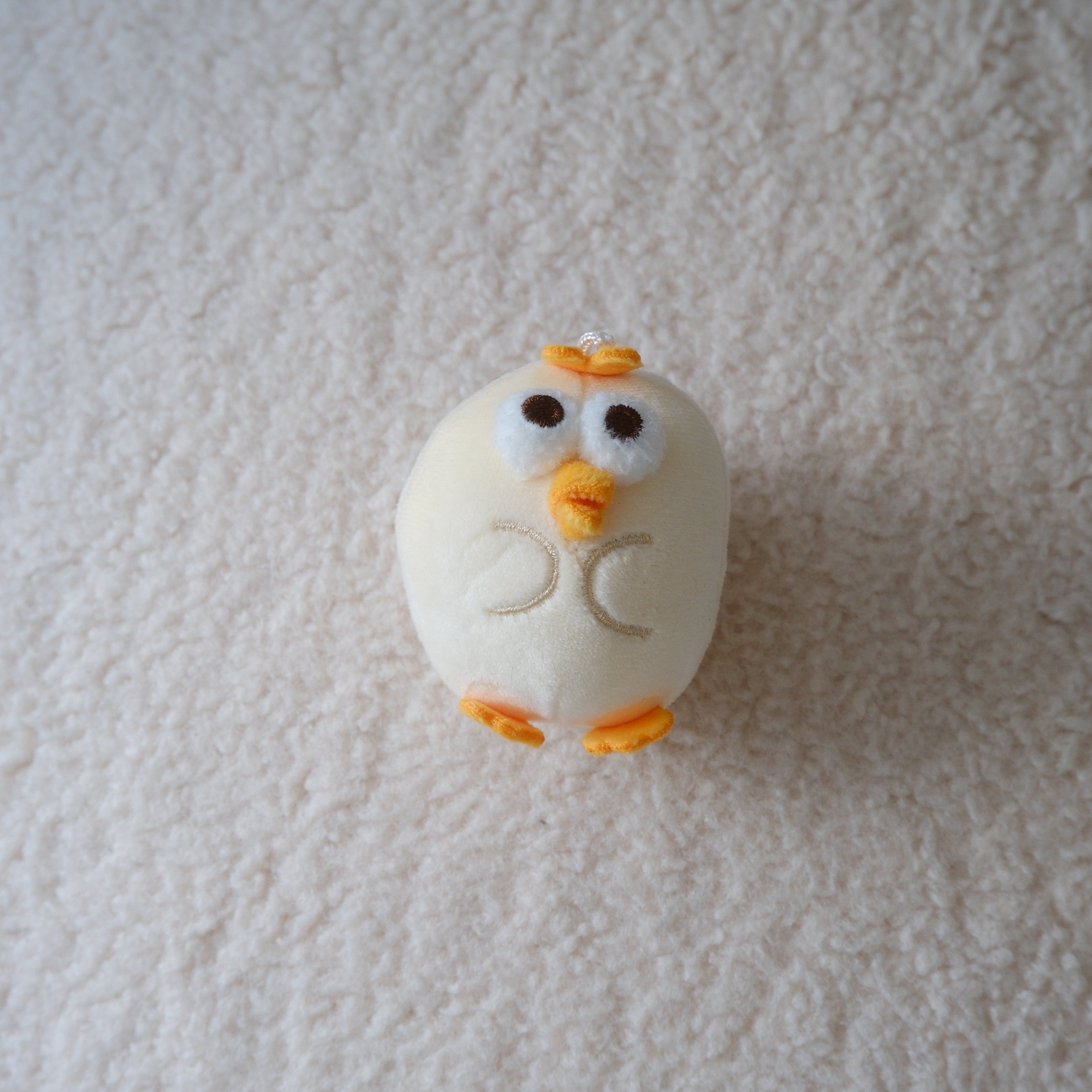 A small white chick figurine with orange beak and feet placed on a textured white fabric background.