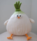 A cute, round plush toy designed like a cartoon onion character, featuring a large white body with vertical yellowish lines, green leafy top, orange beak and feet, and small white wings, sitting on a textured white surface against a neutral gray background.