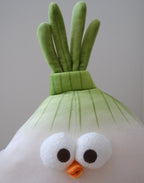 A plush toy shaped like a stylized onion character, with a white body, green leafy top, large white eyes, and a small orange beak, photographed against a plain light gray background.