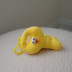 A yellow plush chicken shaped like a key with a small plastic keyring, resting on a textured white surface against a neutral gray background.