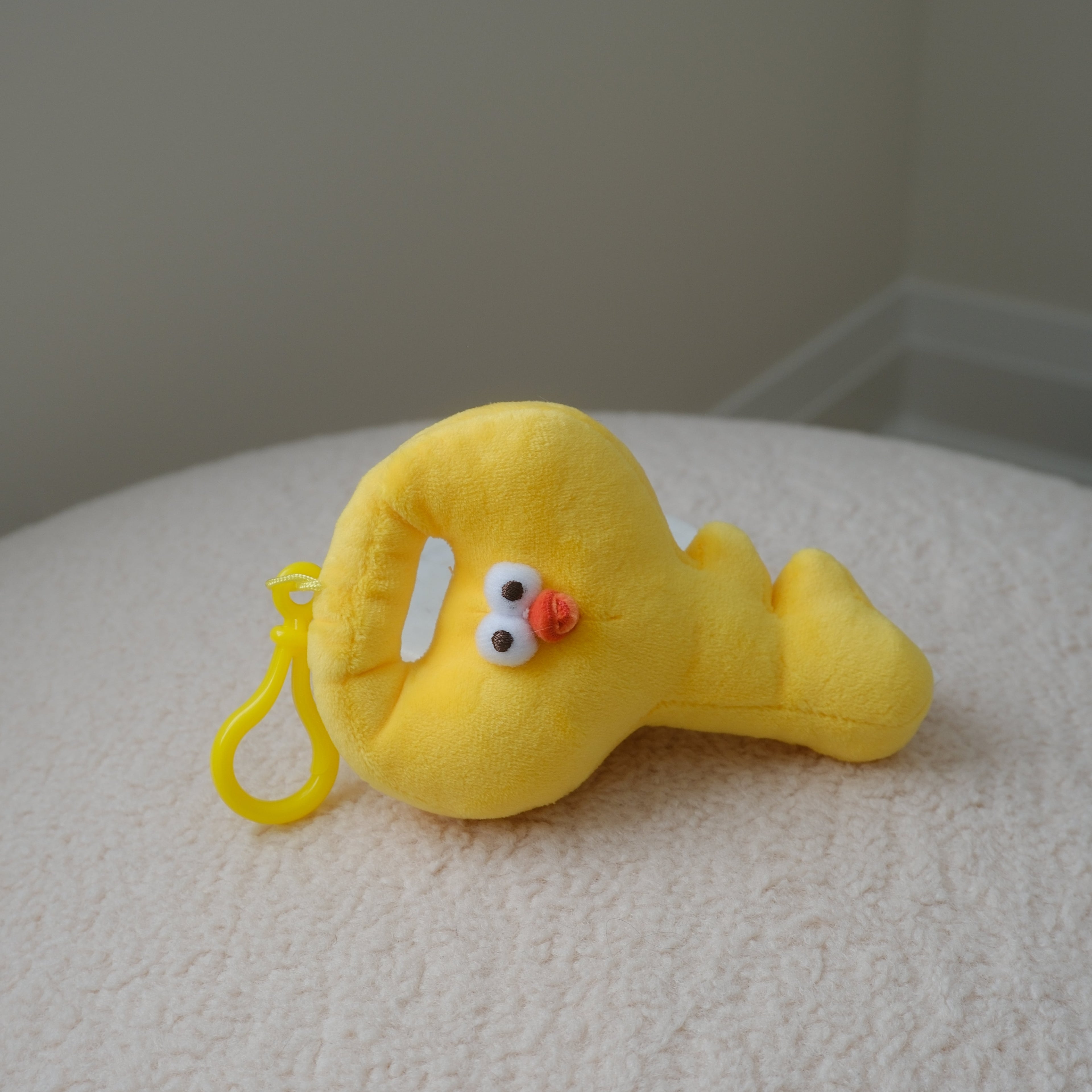 A yellow plush chicken shaped like a key with a small plastic keyring, resting on a textured white surface against a neutral gray background.