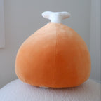 An orange plush shaped like a chicken leg with a white bone, sitting on a textured white surface against a plain light gray wall.