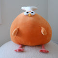 An orange plush toy shaped like a round drumstick with a white bone on top, white eyes, a small yellow beak, peach-colored hands, and pink feet, sitting on a white textured surface against a plain light gray wall.