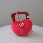 A red plush heart-shaped lock resting on a white textured surface against a neutral gray background. A 'MINISO' brand tag is visible on the side.