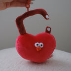 A red heart-shaped lock plush keychain with a curved brown handle, held by a hand. The plush has a cute cartoon face with white eyes and a small orange beak, and is attached to an orange plastic clip.