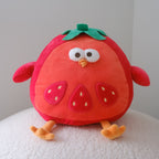 A cute tomato plush toy with a red body, green leafy top, embroidered facial features, and orange feet, sitting on a white textured surface against a plain light gray wall.