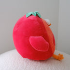 A red plush toy shaped like a tomato, sitting on a white textured surface against a plain light gray background.