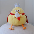 A yellow plush chicken toy with orange feet and beak, wearing a red cape and white crown, holding a fluffy ice-cream cone and sitting on a white textured surface against a plain light gray wall.