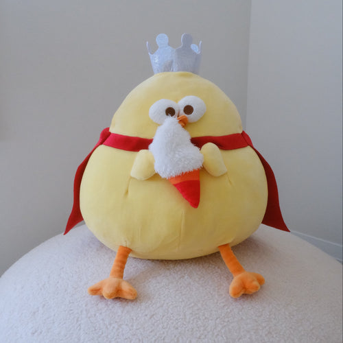 A yellow plush chicken toy with orange feet and beak, wearing a red cape and white crown, holding a fluffy ice-cream cone and sitting on a white textured surface against a plain light gray wall.