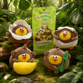 Four plush monkeys arranged on moss in a forest-like setting, alongside a bright green pouch labeled 'Surprise Bag' and 'Dundun Monkey.' The scene includes leaves, logs, and natural props, making this a lifestyle-style product display rather than a plain studio shot.
