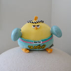A yellow plush toy chicken with turquoise boxing gloves, wearing a black-and-white striped headband and a light turquoise shorts with the word 'DUNDUN' in yellow, sitting on a white textured surface against a plain light gray wall.