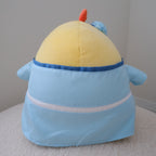 A plush toy shown from the back. It wears a light blue robe with a white horizontal stripe and a blue dome-shaped hat.