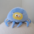A cute blue octopus plush toy with a yellow face, resting on a textured white surface against a plain light gray wall.