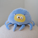 A cute blue octopus plush toy with a yellow face, resting on a textured white surface against a plain light gray wall.