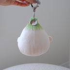 A hand holds a small plush character keychain shaped like a cute white and green onion with orange feet and beak, attached to a silver metal clasp.