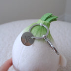 A white plush onion keychain with green fabric leaves and a silver metal keyring and key tag, held by a hand against a soft neutral background.