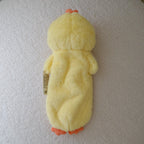 A yellow plush chicken with orange beaks and feet, lying on its back on a round, textured off-white ottoman.