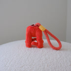 A bright red textured dog toy shaped like a small stool with a red wrist strap, placed on a white textured surface against a plain light gray wall.