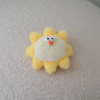 A small plush sun toy with yellow rays, a cream center, and a cute face, resting on a textured cream-colored surface.