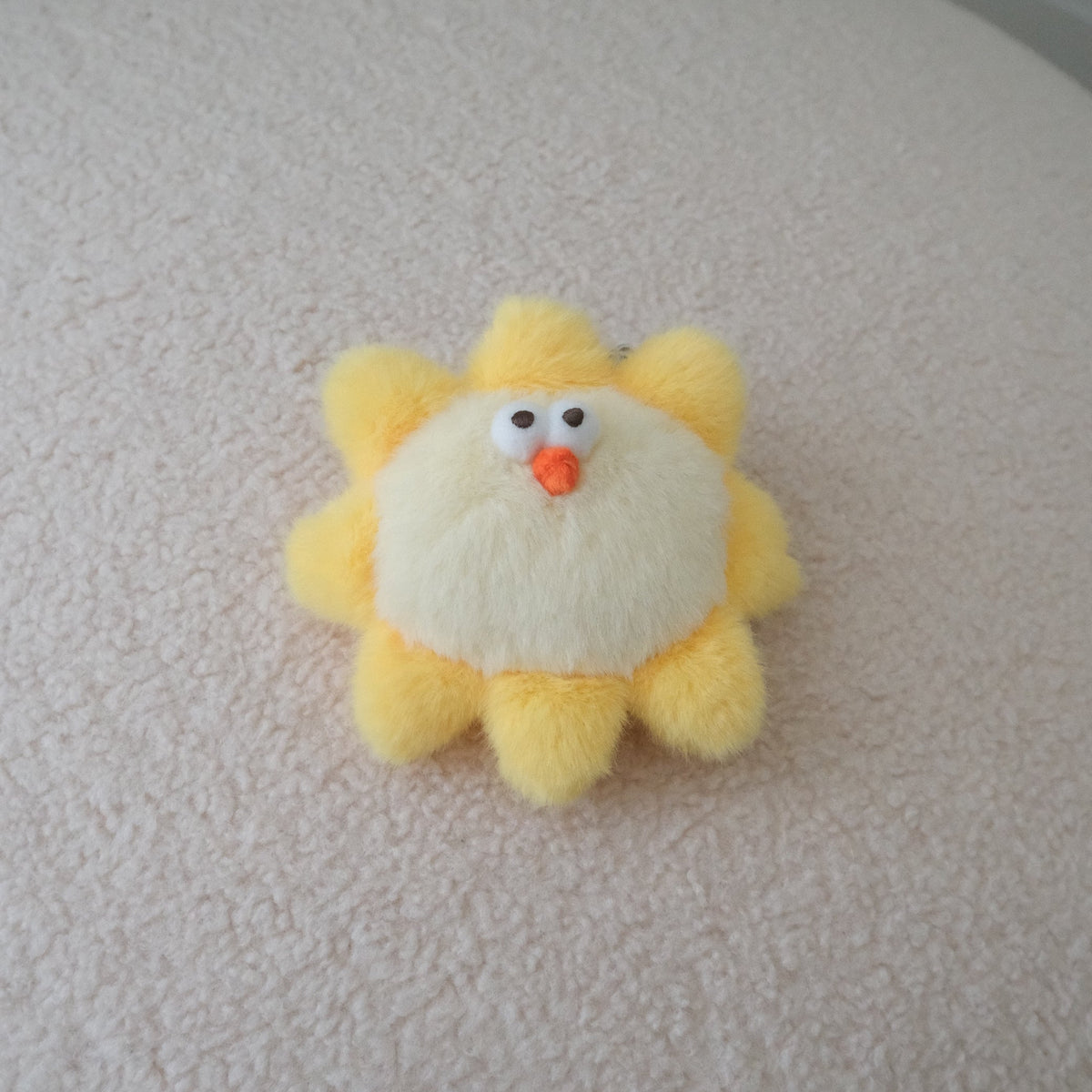 A small plush sun toy with yellow rays, a cream center, and a cute face, resting on a textured cream-colored surface.