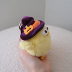 A small yellow plush chick keychain held in a hand, wearing a purple witch hat with an orange pumpkin accent.